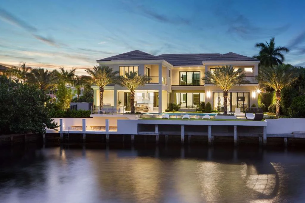 A luxurious waterfront residence with illuminated palm trees at dusk
